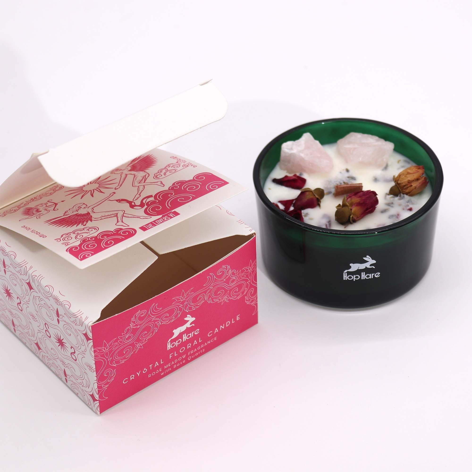 A green candle with decorative elements next to a pink box with branding on a white background