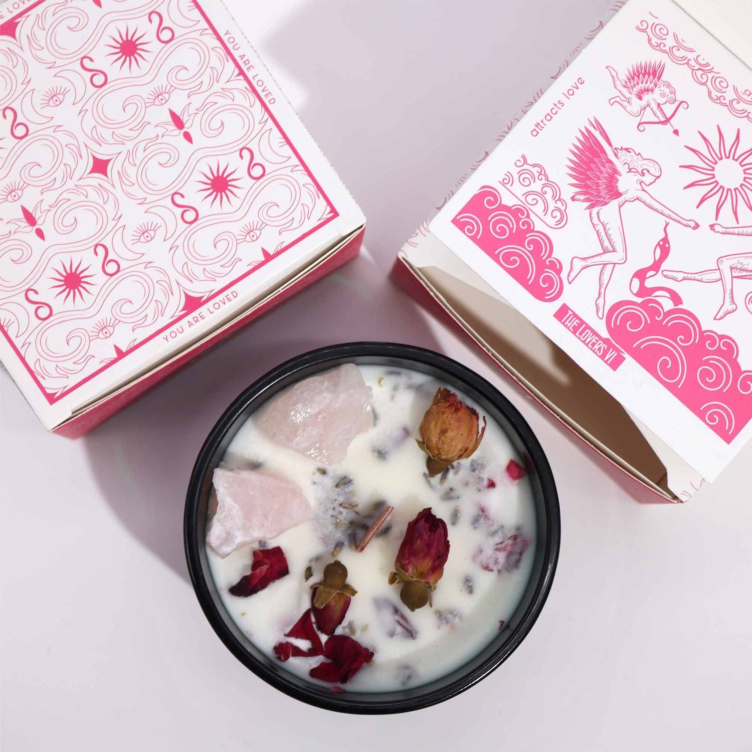 Candle with dried flowers in a dark green container next to pink boxes on a light background