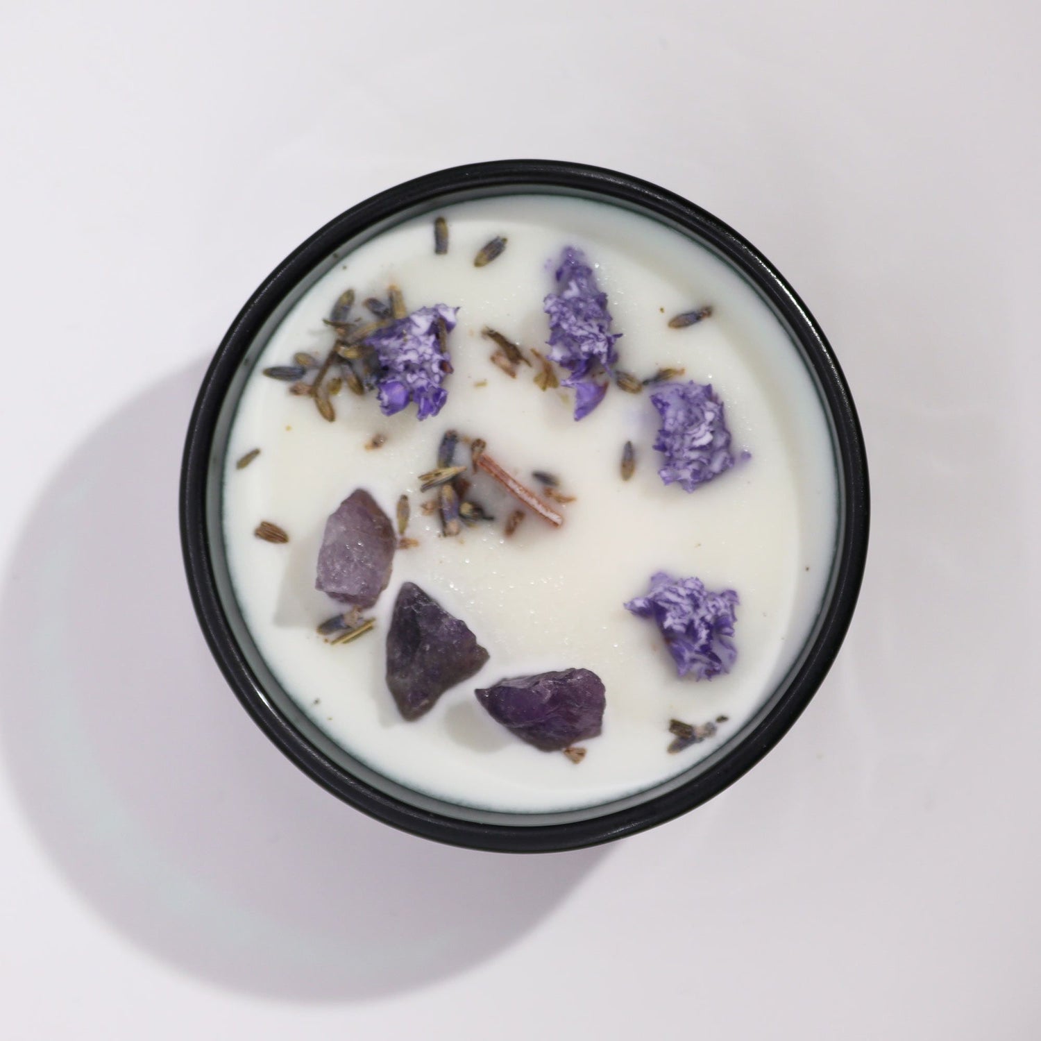 Candle with lavender pieces in a dark green container on a white background
