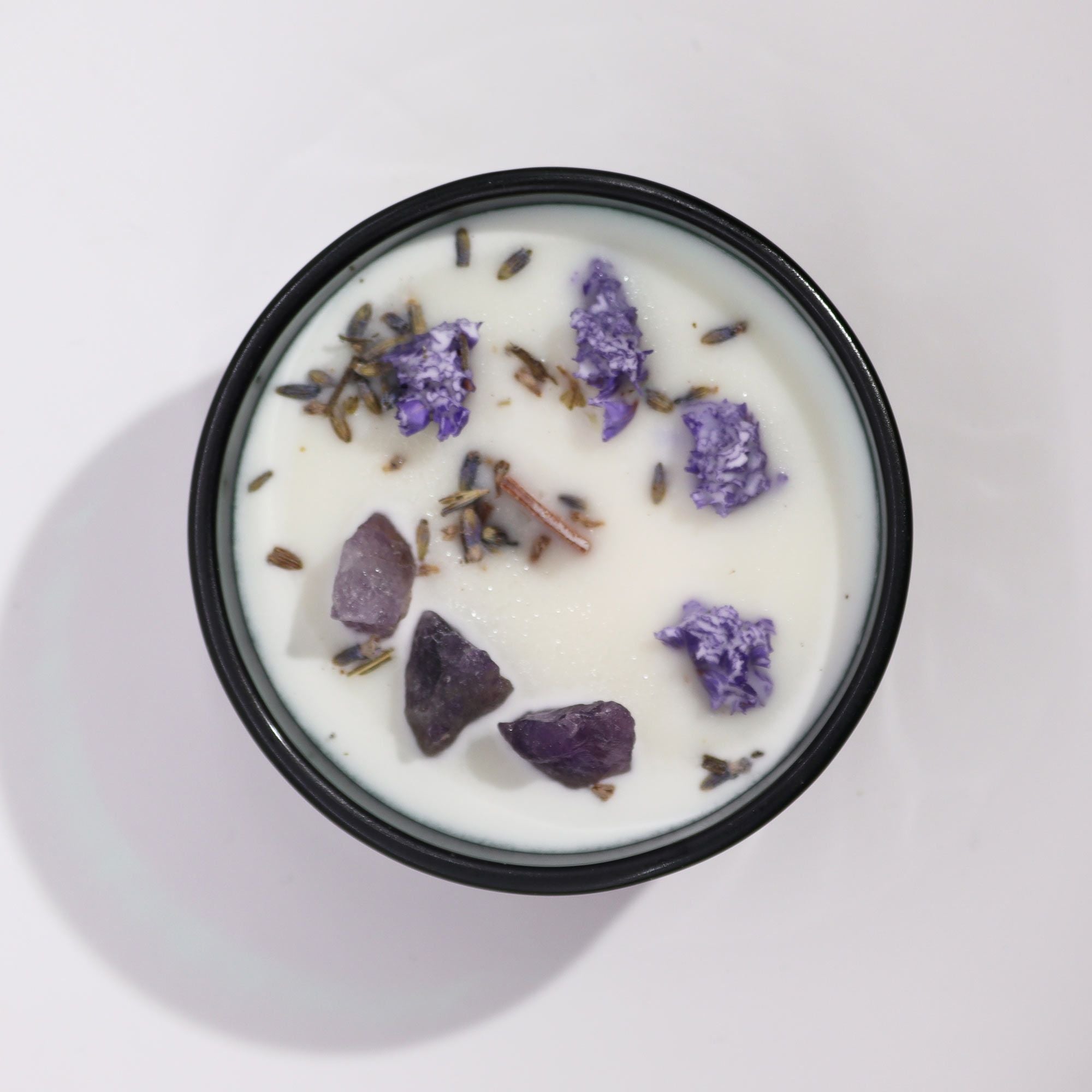 Candle with lavender pieces in a dark green container on a white background