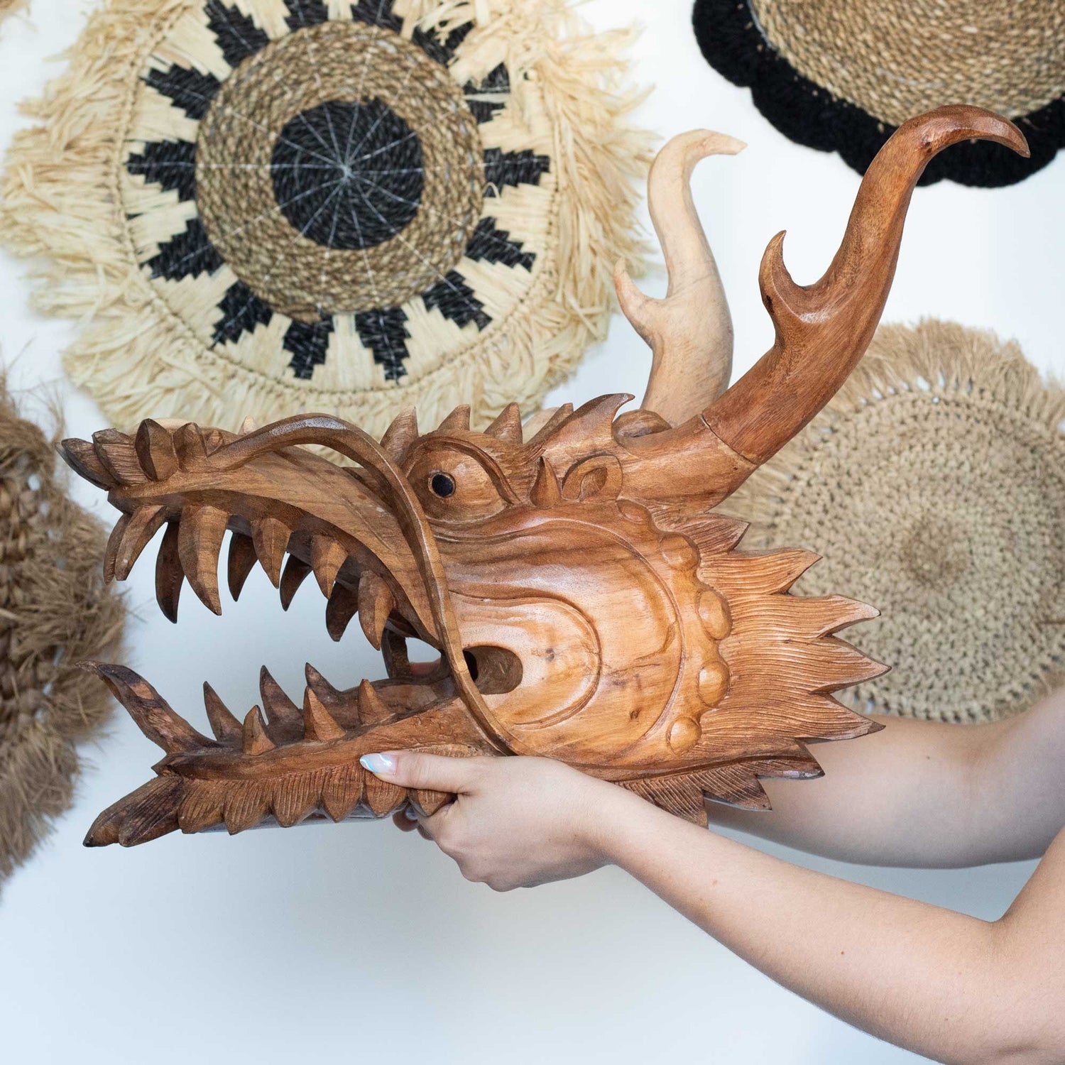 A wooden dragon head sculpture held by a hand with woven mats in the background