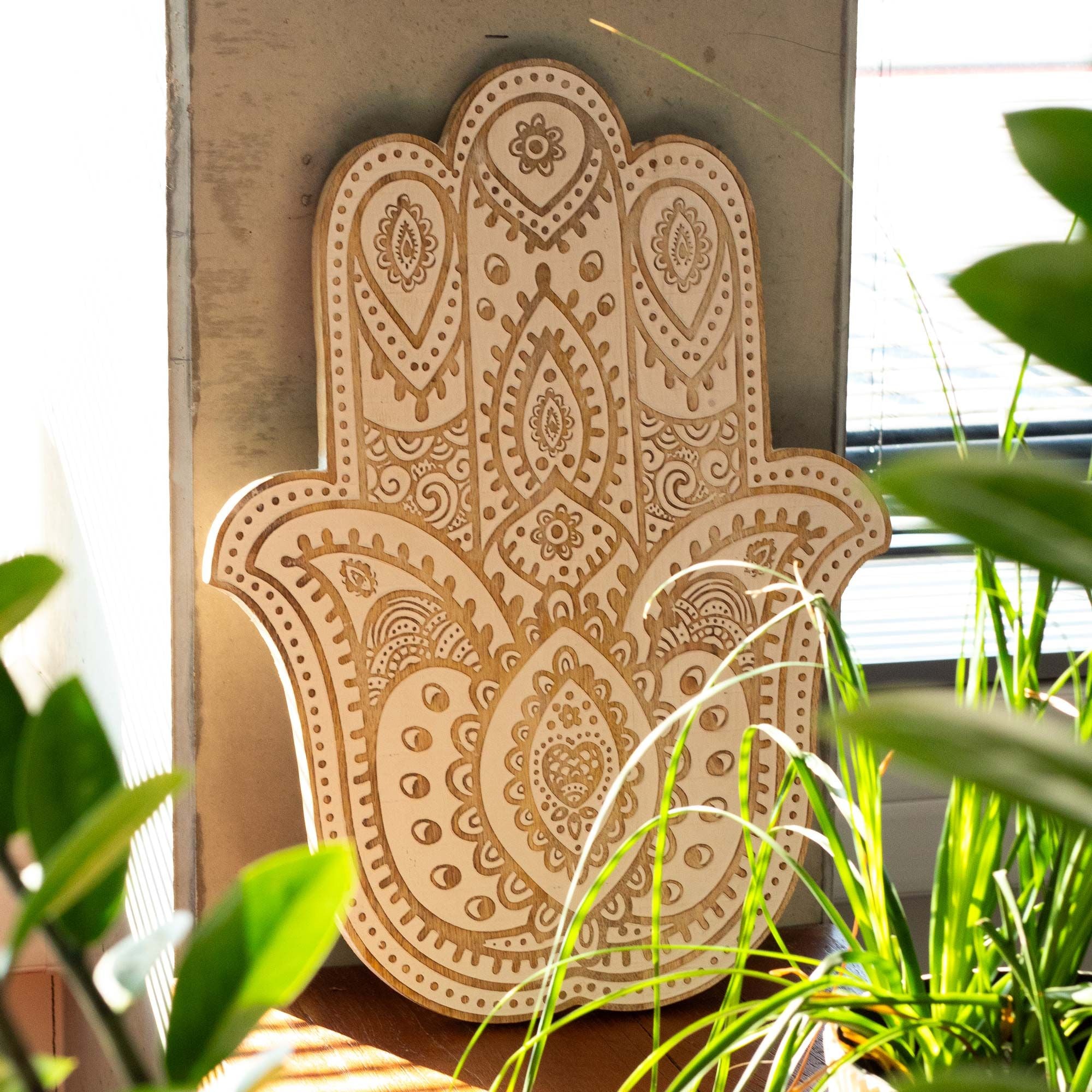 Decorative Hamsa hand wall art with intricate patterns, surrounded by green plants.
