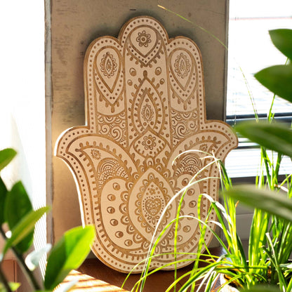 Decorative Hamsa hand wall art with intricate patterns, surrounded by green plants.