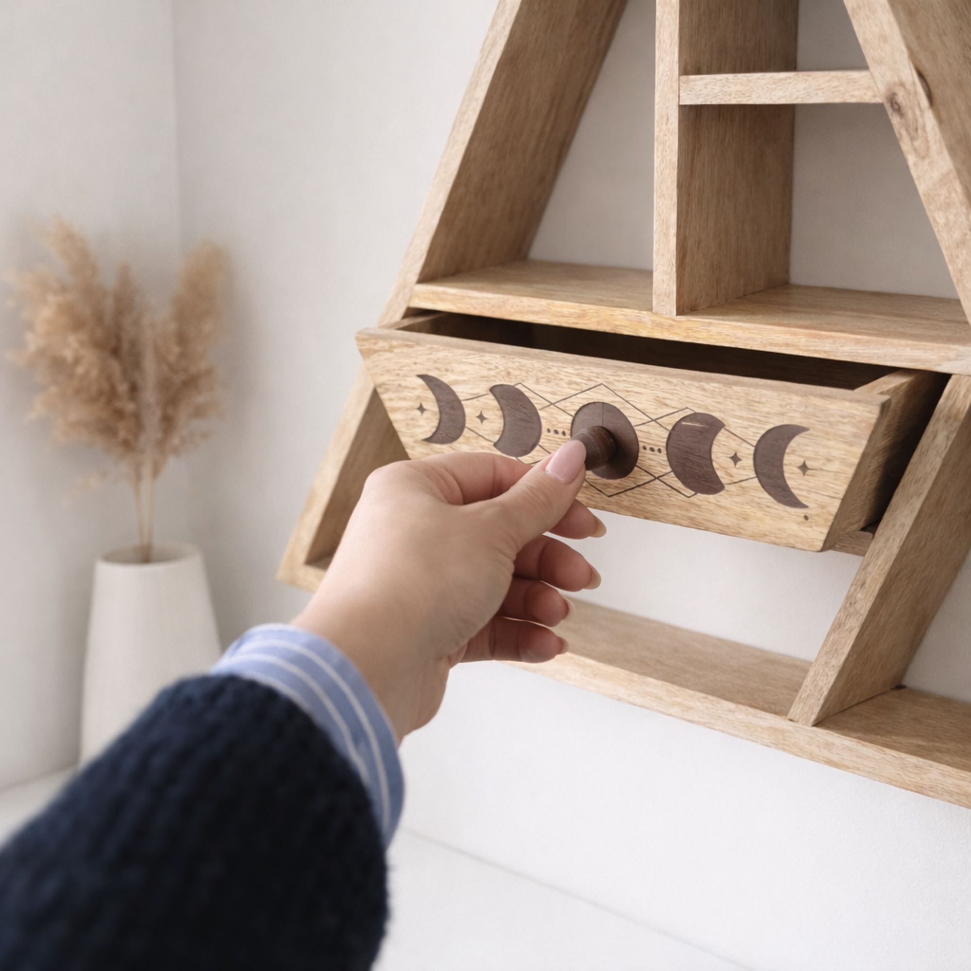 Wooden shelf with a hand opening a drawer featuring moon phase design, with a neutral background.