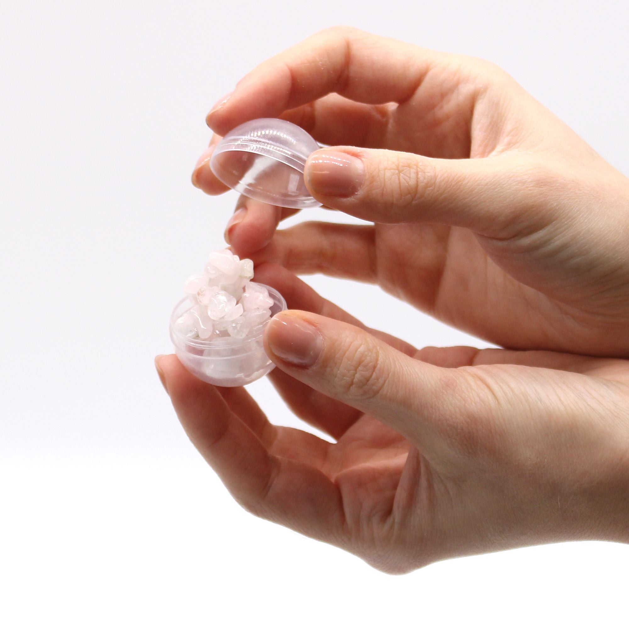 Hand holding a small transparent container with a white bracelet on a light background