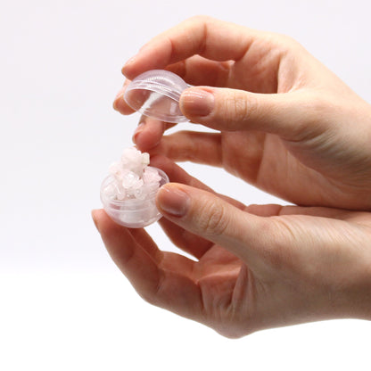 Hand holding a small transparent container with a white bracelet on a light background