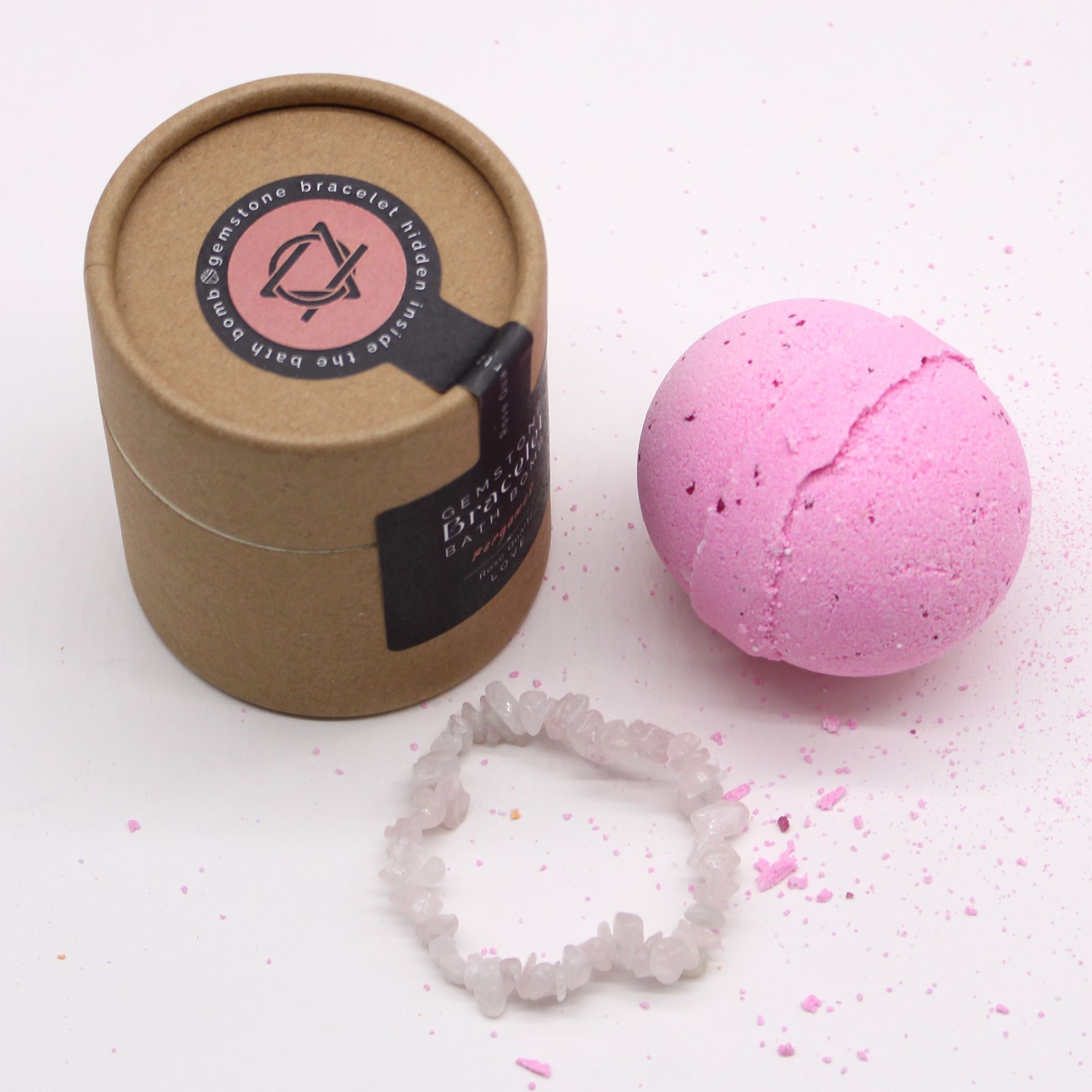 Pink bath bomb with a brown cardboard container and crystal bracelet on a white background