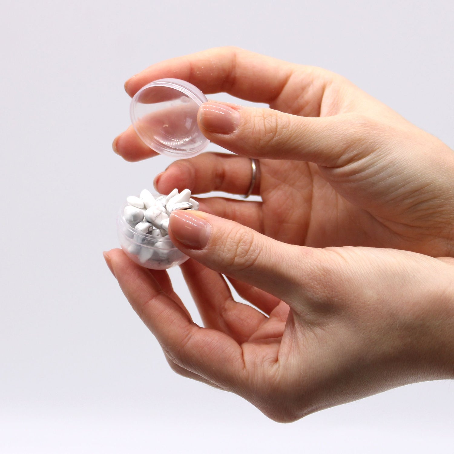Hand holding a small container with a white bracelet against a light gray background